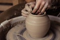 Close-up view on dirty man hands of potter creating with fingers and pressure an earthen jar pot of white clay on the potter`s whe Royalty Free Stock Photo