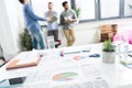 Close-up view of documents and business charts on desk and businessmen standing behind Royalty Free Stock Photo