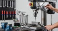 Close-up View of Drill Press in Workshop Environment with Metallic Tools and Equipment on Wall and Hands Operating the Machine Royalty Free Stock Photo