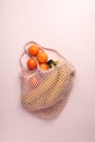 Close-up view of eige string bag with ripe tropical fruits on pink pastel background, summertime blogger style vegan vegetarian