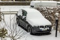 Close-up view of electric car BMW iX3 with charging cable in parking lot of private house covered with snow on winter day.