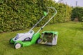 Close-up view of electric lawn mower with basket of cut grass standing on trimmed green lawn in garden of private villa. Royalty Free Stock Photo