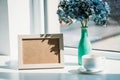 close up view of empty photo frame, cup of coffee and bouquet of hortensia flowers in vase on windowsill Royalty Free Stock Photo