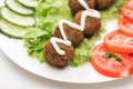 Close up view of falafel with sauce on plate with sliced vegetables on white background.