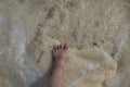 Close up view of feet with sunburn marks of man standing on sandy coast with incoming waves. Royalty Free Stock Photo