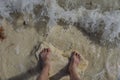Close up view of feet with sunburn marks of man standing on sandy coast with incoming waves. Royalty Free Stock Photo