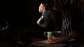 Female barista spills hot coffee from coffee pot to cup in dark background