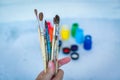 Close up view of female hand with set of paint brushes on blue blurred background with paints cans Royalty Free Stock Photo