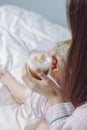 Close up view female hands holding cup of hot coffee or cappussino in the morning. Attractive girl in pajamas relaxes