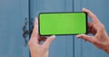 Close up view of female hands holding smartphone with green tamplate screen horizontally. Concept of mockup and chroma