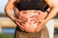 Close-up view of four hands on the abdomen of a pregnant adult woman standing outdoors