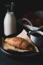 Close up view of fresh baked croissant wrapped on piece of paper with a fresh hot coffee cup on a black plate  with bottle of milk Royalty Free Stock Photo