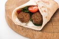 Close up view of fresh falafel balls in pita with vegetables and sauce on wooden board on white background.