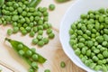 Close-up view of freshness green peeled peas collected in white plate and scattered on light wooden table Royalty Free Stock Photo