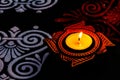 Close up view of glowing diya with white and red rangoli art on black background. diwali cencept