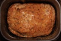 Close-up view of golden-crusted wheat bread with seeds in a metal bread maker container. Homemade bread.