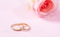 Close up view of golden wedding rings and a blurry pink rose, copy space, on a pink background. Royalty Free Stock Photo