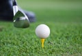 Close-up view of a golf ball set on a wooden golf tee in the grass with a golf club positioned behind it as though about to hit Royalty Free Stock Photo