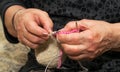 Close-up view of grandma`s hands holding knitting needles while sitting on the sofa, creating something with her own