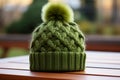 A close up view of a green crocheted beanie with a faux fur pompom.