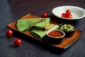 Close up view green tortilla quesadilla with chicken, cheese on a brown plate with red sauce on a wooden background. mexican