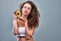 Close up view half naked woman with perfect skin nude hold in hand fresh ripe avocado on grey background studio portrait