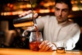 Close-up view of hand of bartender holds shaker with strainer and pours steaming drink into glass.