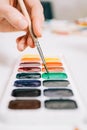 Close-up view of hand holding a brush and mixing the colors of paints on palette. Concept of art education, art class or studio