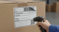 Close-Up View of a Hand Scanning a Shipping Label on a Cardboard Box in a Warehouse Environment Royalty Free Stock Photo
