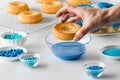 Close up view of a hand about to dip a donut into melted blue chocolate.