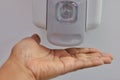 Close-up view of hand under an automatic wall mounted sanitiser dispenser.