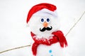 Close-up view of handmade snowman with a scarf, Santa Claus hat, carrot nose and mustache in a snowy park Royalty Free Stock Photo