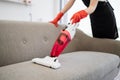 Close up view of hands of cleaner vacuuming sofa with portable vacuum cleaner. Royalty Free Stock Photo