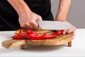 Close-up view of the hands of a male cook who cuts red chili peppers with a knife on a cutting board Royalty Free Stock Photo