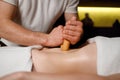 Close up view hands of a strong masseur massage the female abdomen with bamboo sticks.