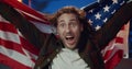 Close up view of handsome young man sitting in front of tv and supporting favourite team. Long haired guy with USA flaf