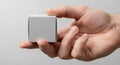 a close up view of a human hand holding a small blank white rectangular box against a neutral gray background Royalty Free Stock Photo