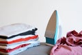 Close up view of iron clothes on ironing board with stack of ironed shirts