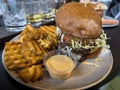 Close up view of a juicy cheeseburger with a side of crispy waffle fries with a whiskey flight on the table behind it