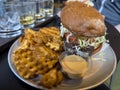 Close up view of a juicy cheeseburger with a side of crispy waffle fries with a whiskey flight on the table behind it