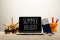 close up view of laptop with summer holiday lettering, sea star, sunglasses, passports with tickets and toy bucket on sand on grey