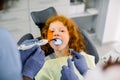 Close up view of little girl patient having dental treatment at dentist`s office. Hands of two female dentists making