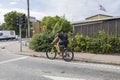 Close up view of man on bicycle waiting on red stop light. Green plants and buildings on blue sky and white clouds background.