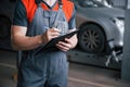 Close up view. Man at the workshop in uniform using notepad for his job for fixing broken car Royalty Free Stock Photo