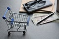 Close-up view model shopping cart on table desk with money, pencil, glasses and notebook.