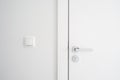 Closed door with metal handle and lock close to light switch on white wall Royalty Free Stock Photo