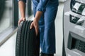 Close up view. Moving the tire. Man in blue uniform is working in the car service Royalty Free Stock Photo