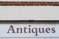 Close-up view of a painted, Antiques sign seen pained on a white washed, brick wall in an English village.