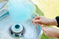 Close up view of person hands spinning blue color cotton candy with machine.