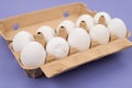 Close up view photo of cardboard container with ten and one broken white chicken eggs  isolated purple background Royalty Free Stock Photo